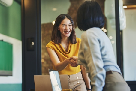 Cheerful businesswomen shaking hands in meeting room stock photo